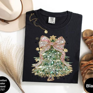Könnte beinhalten: Schwarzes T-Shirt mit Rundhalsausschnitt und einem Weihnachtsbaum-Design. Der Baum ist mit rosa und silbernen Strasssteinen und einer großen rosa Schleife verziert. Das Shirt hat ein Comfort Color Brand-Etikett und ist schwarz.