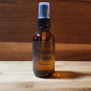 May include: A brown glass spray bottle with a black and clear spray nozzle. The label reads "Flame's Enchantments Candle Co. Vanilla Bean Room Spray."