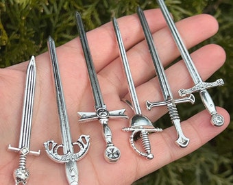 Peut inclure: Six épées miniatures en argent avec des détails complexes, notamment une croix, une couronne et un casque. Les épées sont présentées sur une main.