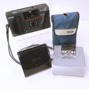 May include: A black Ricoh AF-50/70 camera with a close-up adapter, a black leather camera case, and a blue Ricoh camera bag.