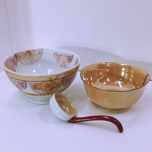 May include: A set of three ceramic bowls, one large with a floral design, one smaller with a gold glaze, and a white ladle with a red handle.