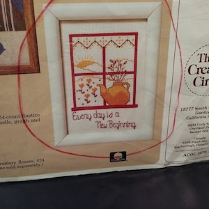 May include: Cross stitch pattern featuring a window with a teapot and flowers inside. The text "Every day is a New Beginning" is below the window. The pattern is from The Creative Circle and is called "ACOC 1678".