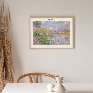 May include: A framed print of a painting by Claude Monet titled "Spring by the Seine (Lily Pond)". The painting depicts a river scene with a group of people on the bank, a boat on the water, and a building in the distance. The sky is a light blue with white clouds.