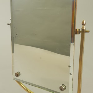 May include: A vintage brass and marble tabletop mirror with a bevelled glass mirror. The mirror is attached to a brass stand with a marble base. The mirror can be adjusted to different angles.