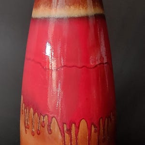 Pode incluir: Um vaso de cerâmica alto, em forma de gota, com acabamento brilhante. O topo é marrom quente, transicionando para um vermelho vibrante com detalhes escorridos. A base é marrom claro. O URL da loja Etsy é visível.