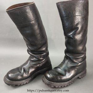 May include: A pair of black leather knee-high boots. The boots have a textured appearance and a rugged sole. The boots are vintage and show signs of wear. The boots are approximately 16 inches tall.