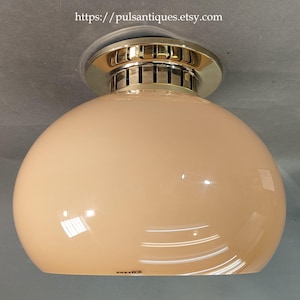 Könnte beinhalten: Eine Vintage-Deckenleuchte mit einem pfirsichfarbenen, abgerundeten Glasschirm. Die Leuchte hat eine goldfarbene Metallverkleidung und einen silberfarbenen Sockel. Der Text "https://pulsantiques.etsy.com" ist oben im Bild zu sehen.