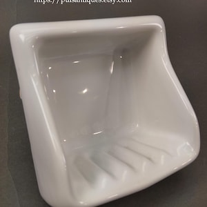 Può includere: Un portasapone in ceramica bianca con un bacino rettangolare e lati curvi. Il portasapone presenta scanalature parallele sul fondo per il drenaggio. L'URL del negozio Etsy è visibile.