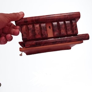 Op de afbeelding: Een houten puzzeldoos met een sleutelgat en een sleutel. De doos is gemaakt van donker hout met een roodbruine tint. De doos is open en de bovenkant is opgetild.