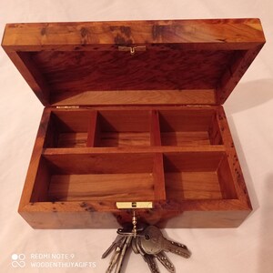 May include: A wooden box with a hinged lid and multiple compartments inside. The box is made of a dark wood with a natural grain pattern. A set of keys is hanging from the box.