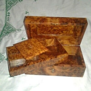 Puede incluir: Una caja de madera con un acabado de madera de raíz. La caja tiene una tapa con bisagras y un cajón más pequeño en el interior. La caja está hecha de varias piezas de madera que se han unido.