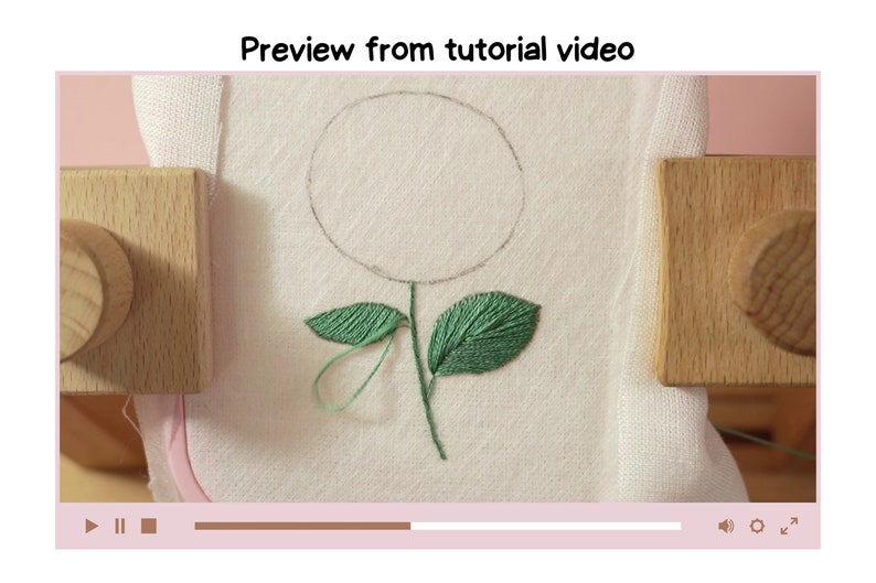 May include: A close-up of a white fabric with a green embroidered flower. The flower has a circle in the center and two leaves. The fabric is stretched over a wooden embroidery hoop.