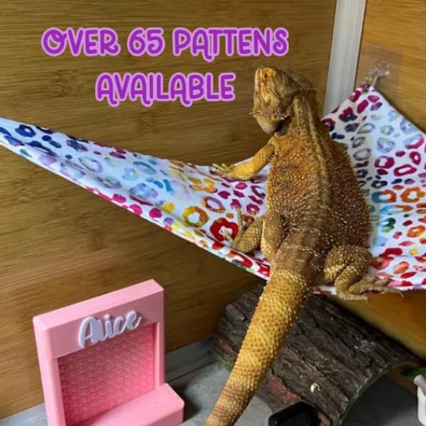 May include: A colourful hammock for a bearded dragon, with a white background and a variety of colourful spots. The hammock is attached to the side of a wooden enclosure. The text "OVER 65 PATTERNS AVAILABLE" is visible in the top left corner of the image.