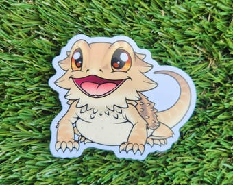 May include: A cartoon sticker of a smiling bearded dragon with orange eyes and a light brown body. The sticker is on a white background.