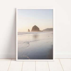 May include: A framed photograph of a rocky island in the ocean. The island is in the distance, and the water is calm and reflective. The sky is a soft blue, and the sand is a light brown.