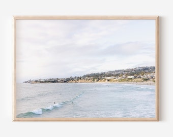 May include: A framed photograph of a beach scene with a coastline in the distance, blue water with white waves, and a light blue sky with white clouds.