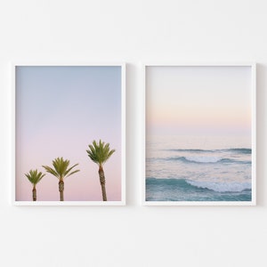 Puede incluir: Dos impresiones enmarcadas, una con un cielo rosa y azul pastel y tres palmeras, la otra con un cielo rosa y azul pastel sobre un océano turquesa con olas.
