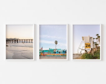 May include: Three framed photographs of a beach scene. The first photo shows a pier extending into the ocean. The second photo shows a colourful building with the words "Pacific Beach" on the side. The third photo shows a lifeguard tower with the number "216" on the side.