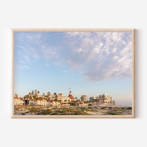 Op de afbeelding: Een foto van een groot wit gebouw met rode daken aan een strand. Het gebouw is omringd door palmbomen en er is een blauwe lucht met witte wolken op de achtergrond.