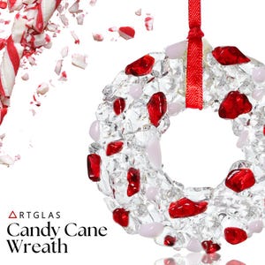 May include: A clear glass wreath with red and pink accents, suspended by a red ribbon. The wreath is decorated with red glass pieces and pink stones. The words "ARTGLAS" and "Candy Cane Wreath" are printed in black.