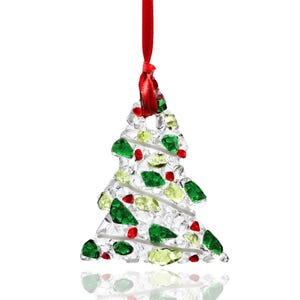 Peut inclure: Une décoration en forme de sapin de Noël composée de morceaux de verre transparent texturé. Le design intègre des fragments incrustés de verre vert, citron et rouge, accentués par de fines spirales de verre blanc. Un ruban rouge est fixé au sommet.