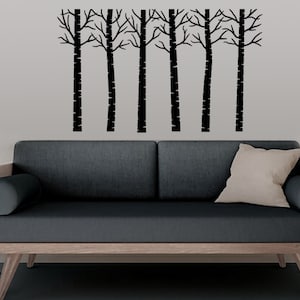 May include: A black silhouette of a row of trees with bare branches against a grey wall above a dark grey sofa with a light brown wooden frame.