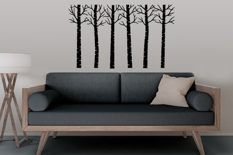 May include: A black silhouette of a row of trees with bare branches against a grey wall above a dark grey sofa with a light brown wooden frame.