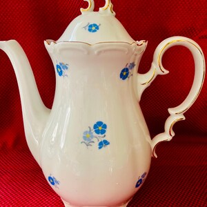 May include: White porcelain coffee pot with a lid, adorned with blue floral patterns and gold trim. The handle and spout are elegantly designed. A classic piece for serving coffee or tea.