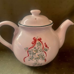 May include: White ceramic teapot with a green trim and a Christmas-themed design featuring a red bow and a red cardinal on a green holly branch.
