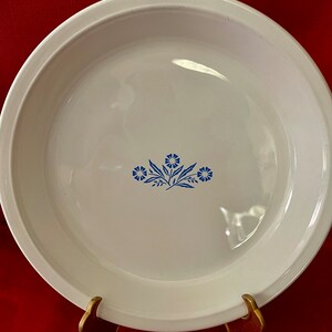 May include: White pie plate with a blue floral design. The design features three stylized flowers with blue leaves.