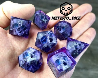 Könnte beinhalten: Satz von sieben lila und weißen Würfeln mit Totenkopf-Design. Die Würfel sind durchsichtig und haben eine glitzernde Oberfläche. Die Würfel liegen auf einer Hand.