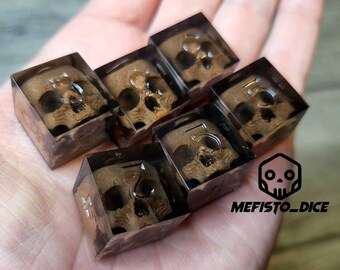 May include: Six clear dice with a skull design inside. The dice are brown and have a translucent appearance. The dice are on a hand.