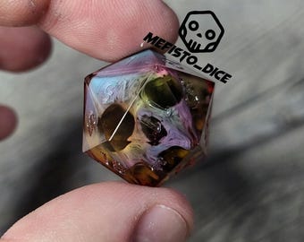 May include: A clear, multi-colored, iridescent, skull-shaped, d20 dice with black numbers. The dice is being held by a finger.