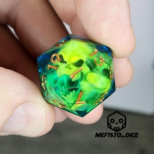Può includere: Un dado fatto a mano a più facce con un design a teschio. Il dado è trasparente con un interno verde e blu e numeri color oro. Il testo "MEFISTO_DICE" è in basso.