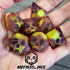 Può includere: Set di sette dadi poliedrici con un designo a forma di teschio. I dadi sono traslucidi e hanno uno schema di colori giallo e viola con glitter incorporati nella resina. I dadi sono realizzati da MEFISTO_DICE.