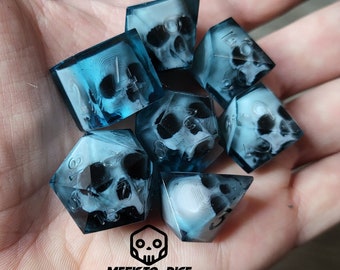 Könnte beinhalten: Satz von sieben blauen und weißen Würfeln mit einem Totenkopfdesign. Die Würfel sind durchsichtig und zeigen das Totenkopfdesign durch das blaue Harz. Die Würfel sind von 1 bis 6 nummeriert.