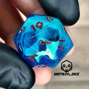 May include: A blue and green d20 dice with red numbers. The dice has a skull design inside.