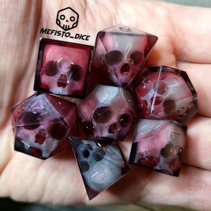 Può includere: Set di otto dadi a forma di teschio di colore viola e bianco con una finitura trasparente e translucida. I dadi sono in una mano, e il testo "MEFISTO_DICE" è visibile sullo sfondo.
