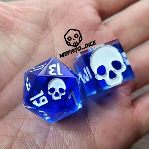 Puede incluir: Dos dados azules con diseños de calaveras blancas. Uno es un dado de 20 caras, el otro es un dado de seis caras. El texto "MEFISTO_DICE" está en la esquina superior izquierda.