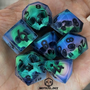May include: Set of seven iridescent dice with a skull design. The dice are a mix of green, blue, and purple colors with black numbers. The dice are made of resin and have a glossy finish.