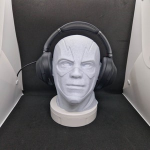 Può includere: Cuffie nere over-ear su una testa di manichino bianca che indossa una maschera bianca con un design a forma di fulmine.