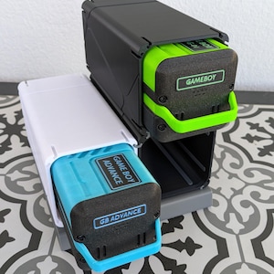 Può includere: Due supporti per cartucce Game Boy Advance. Uno è nero con dettagli verdi e l'altro bianco con dettagli blu. Ogni supporto ha un'etichetta con la scritta "GAMEBOY ADVANCE". I supporti sono su una superficie a motivi.