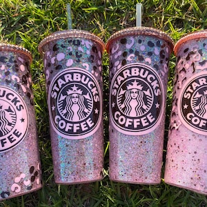 May include: Four pink and black glitter tumblers with a Starbucks logo and the words "Starbucks Coffee" on each. The tumblers have a leopard print design.