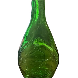May include: A green glass bottle with a round, embossed design. The bottle has a narrow neck and a wide base. The design features a building with a cross on top and the words "The Old Mill" around the edge.