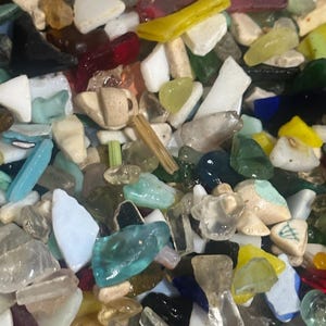 May include: A bowl filled with a variety of colorful, small, broken pieces of glass. The glass pieces are in various shapes and sizes, including squares, rectangles, and triangles. The colors of the glass pieces include blue, green, red, yellow, white, and black.