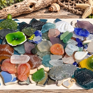 May include: A collection of assorted sea glass pieces in various shapes, sizes, and colors including green, blue, brown, white, orange, and purple. Some fragments feature embossed patterns, while others are smooth, frosted, or translucent.