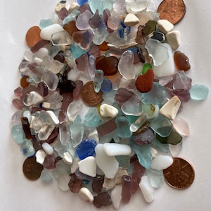 May include: A collection of sea glass in various colors and shapes, including blue, green, white, brown, and purple. There are also several copper pennies scattered throughout the pile.