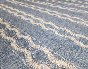 May include: A blue fabric featuring a repeating pattern of white wavy lines running diagonally across the surface. The material has a visible woven texture with a consistent grid-like appearance throughout the entire textile design.