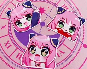 May include: Three pink and black anime-style character stickers with large eyes. The characters are wearing cat ears and have different expressions. The stickers are on a pink and purple background with a clock face.