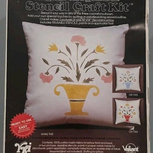 May include: A Stencil Craft Kit packaging featuring a white square pillow with a yellow vase and floral design. The box displays text including Stencil Craft Kit and 14x14 inch decorator pillow, with two smaller inset images showing alternative color schemes.